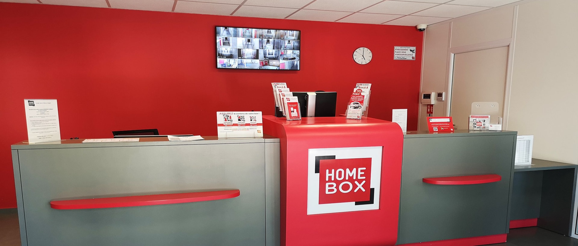Comptoir d'accueil rouge avec logo et écrans de vidéosurveillance, HOMEBOX Strasbourg - Schiltigheim