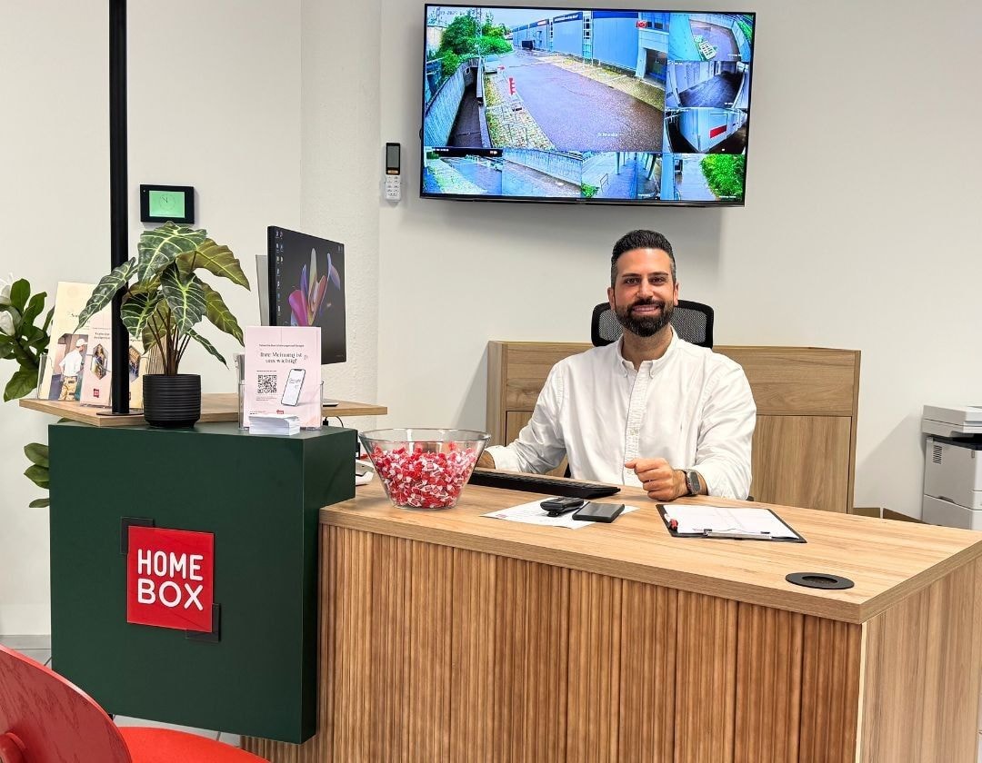 Smiling employee at wooden reception desk with security monitor at HOMEBOX Stuttgart